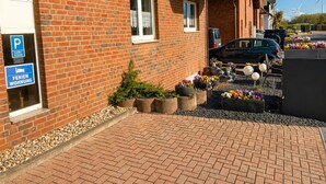 Un bâtiment en briques avec un panneau indiquant un parking, un parterre de fleurs et une voiture garée à l’extérieur.