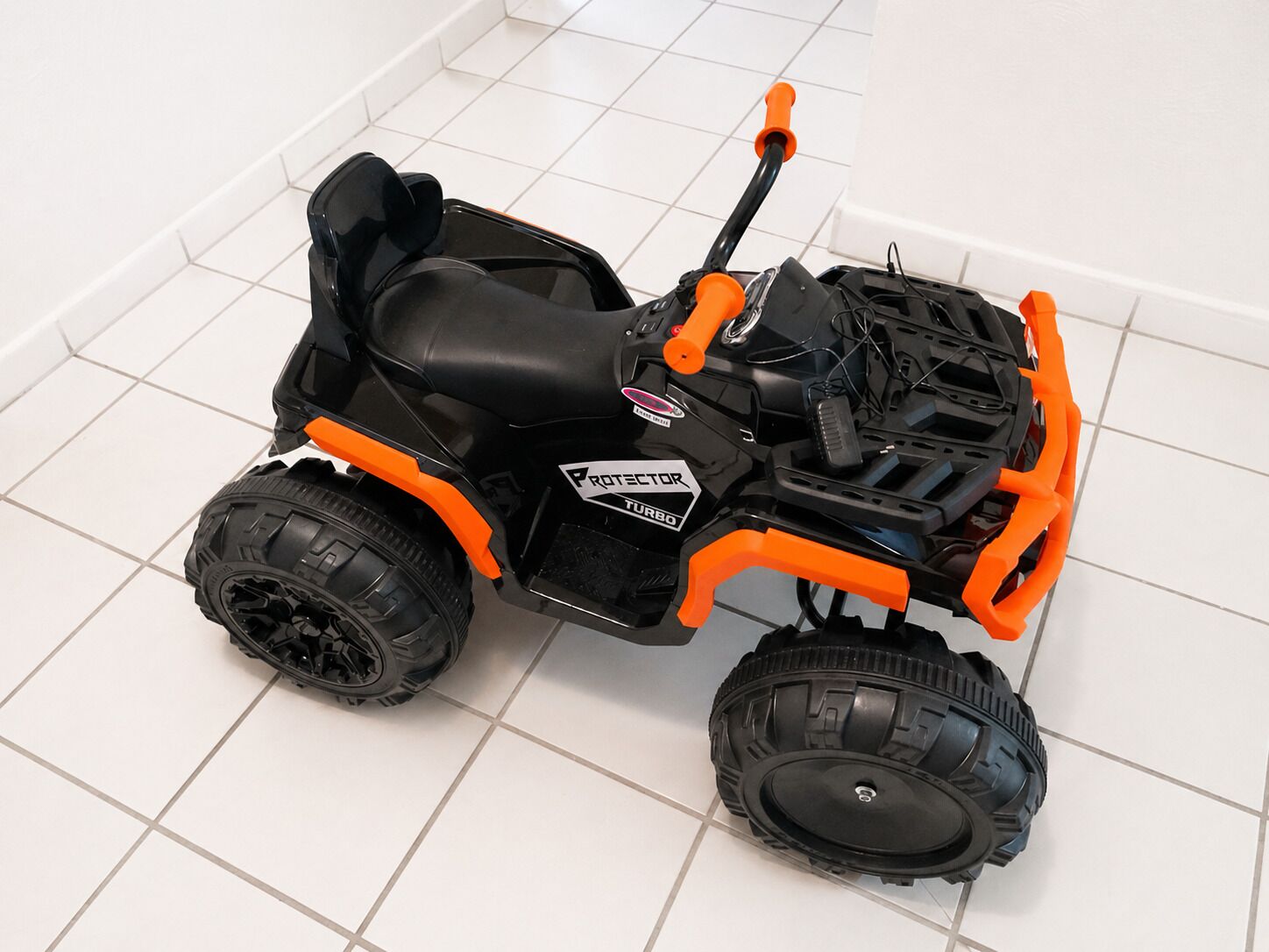 A toy ATV with black and orange colors, a black seat, and a logo on the side.