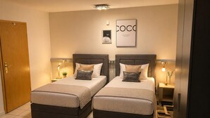 Une chambre avec deux lits, une porte en bois, un tableau encadré et un luminaire fixé au mur.