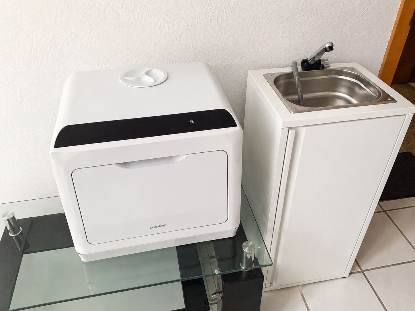 Eine kleine Küchenzeile mit Kaffeemaschine, Spüle und einer Glasablage.