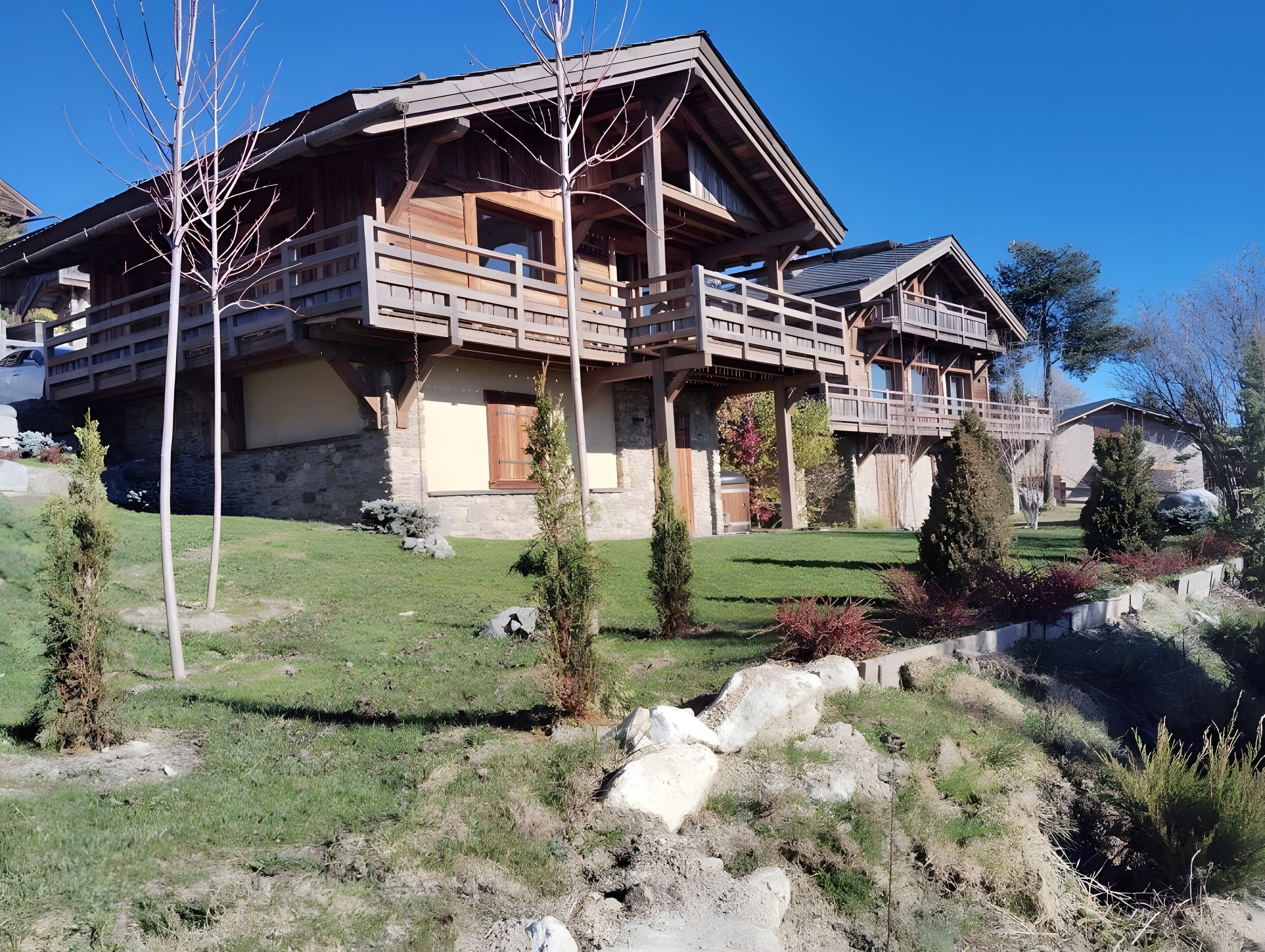 A wooden chalet with a balcony, stone walls, and a well-maintained lawn.