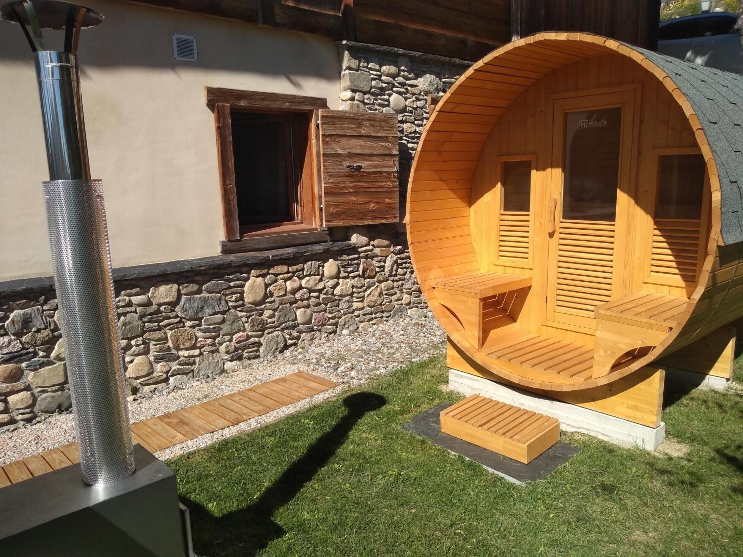 Eine Saunakabine aus Holz mit einer Steinwand und einem Metall-Saunabalken.