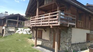 Un chalet en bois doté d’un balcon, de murs en pierre et d’une cour gazonnée.