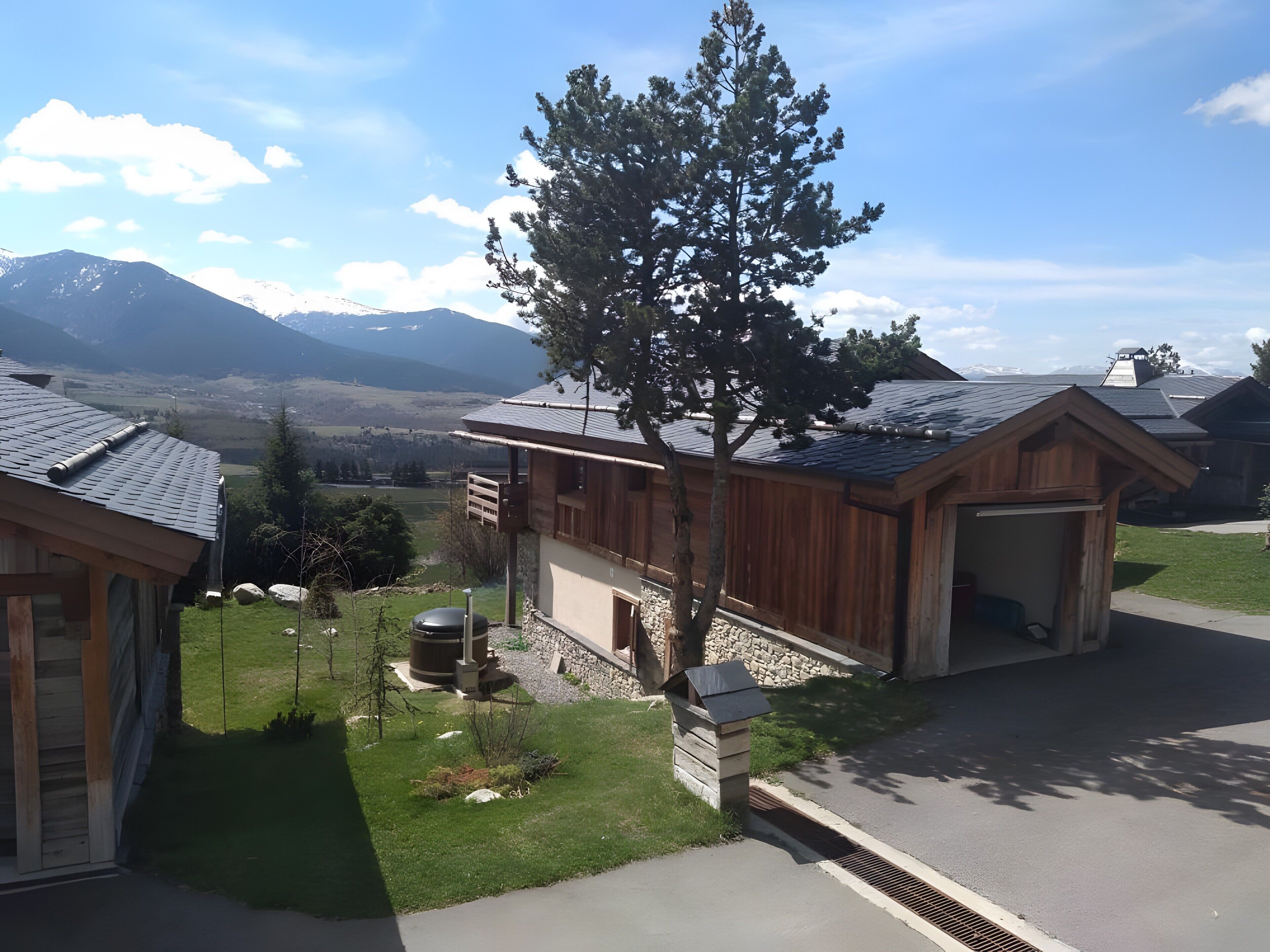 A residential area with wooden houses, a large tree, and a mountain view.