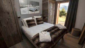 A bedroom with a large bed, wooden walls, a view of the outdoors, and a painting on the wall.
