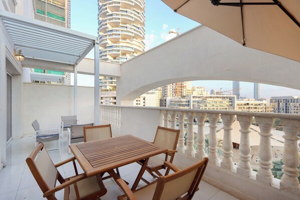 Un balcon avec une table et des chaises en bois, une balustrade blanche et une vue sur les bâtiments environnants.