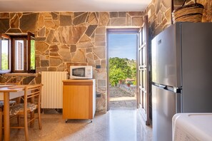 A kitchen with stone walls, a wooden table, a microwave, a refrigerator, and a view of greenery outside. - Trullo 'Dona Filomena' with Private Terrace, Private Garden and Wi-Fi (Selva di Fasano)