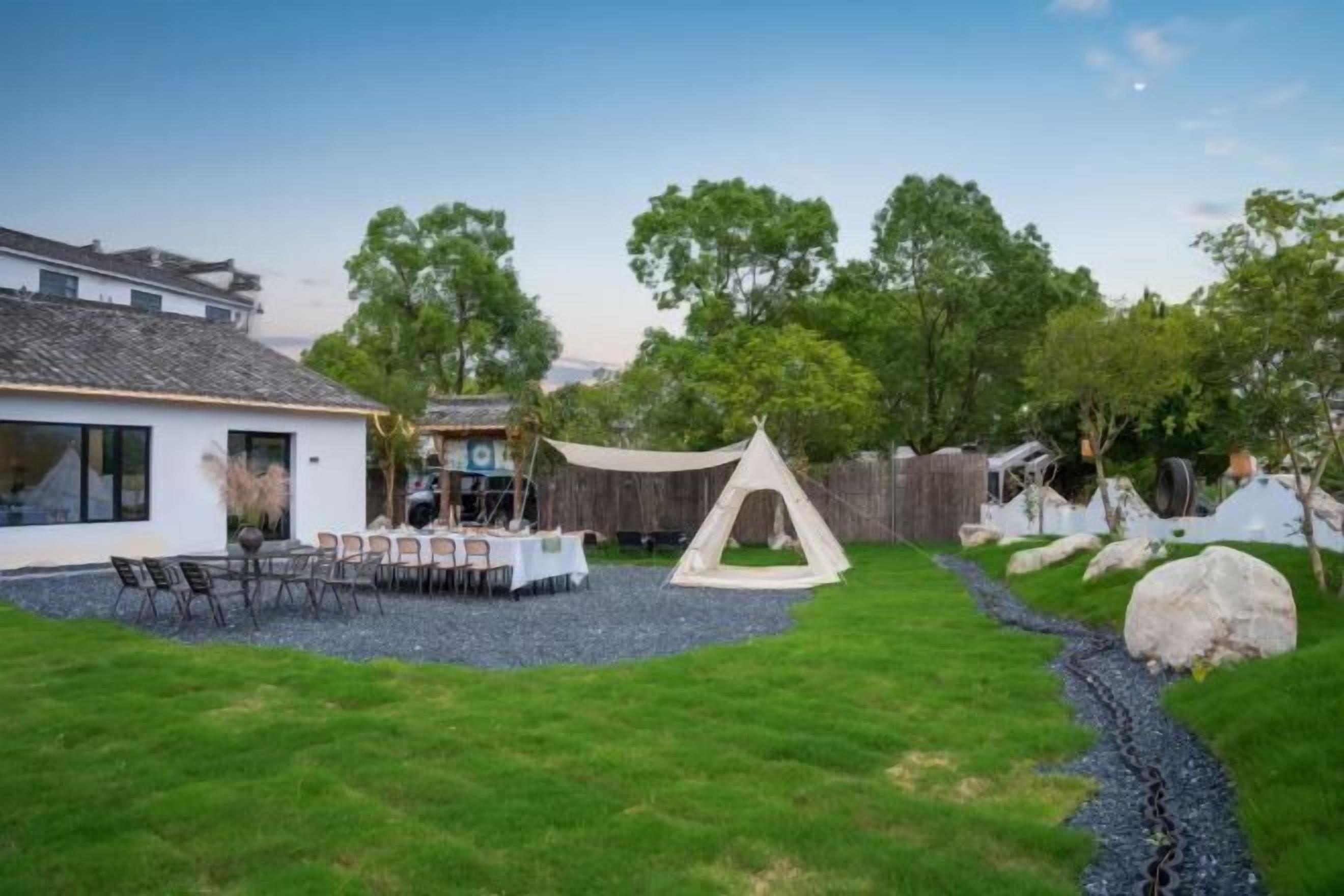 A modern house with a dining area, a tent, and a garden with a gravel path.