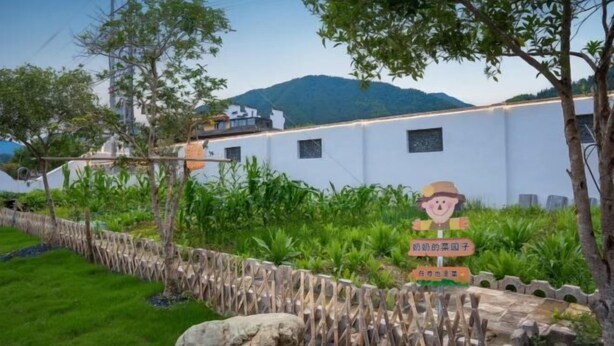 Un edificio blanco con un jardín delantero, un letrero con un personaje de caricatura y una montaña al fondo.
