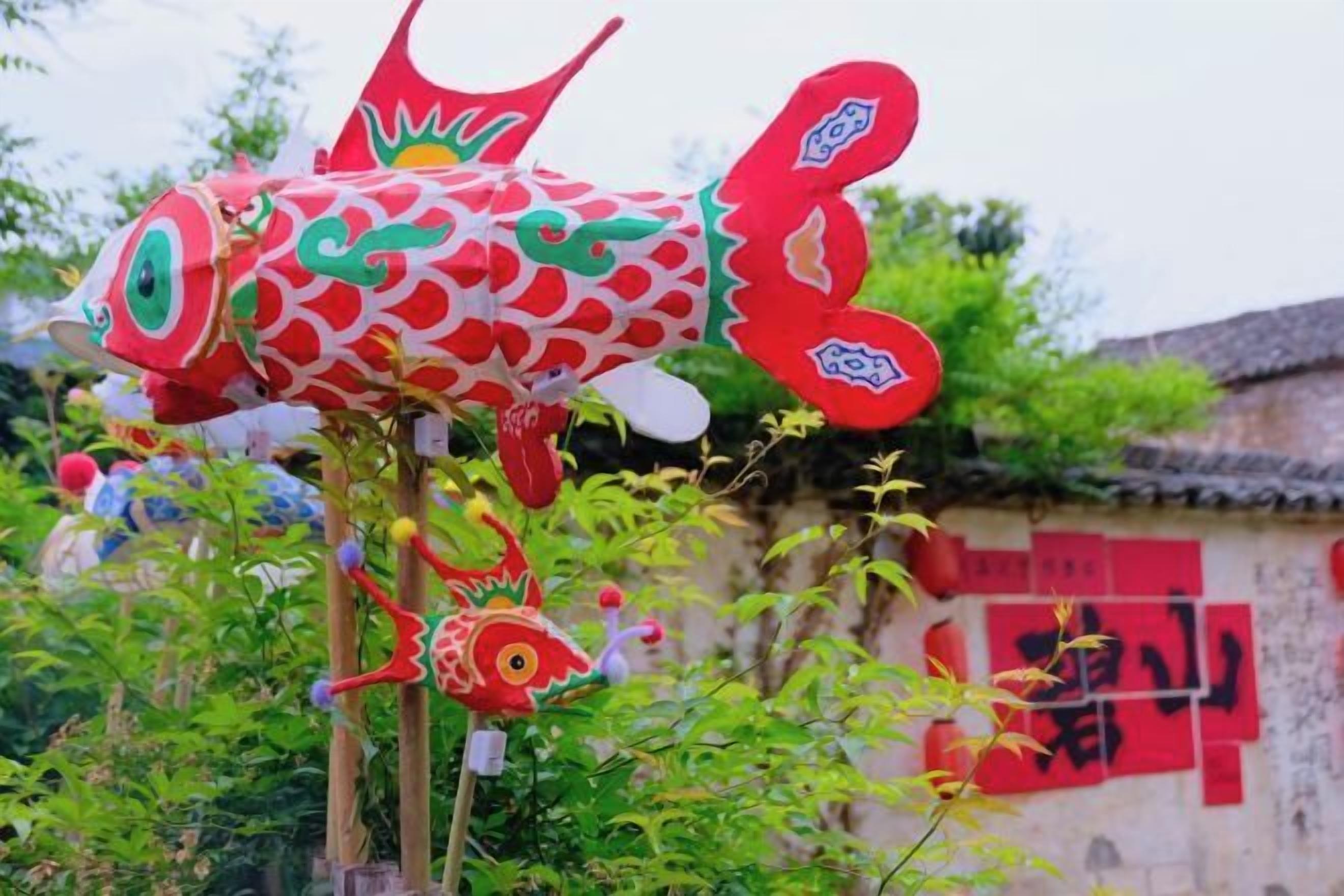 Una escultura decorativa de pez con un diseño rojo y blanco, frente a una pared con caracteres rojos.