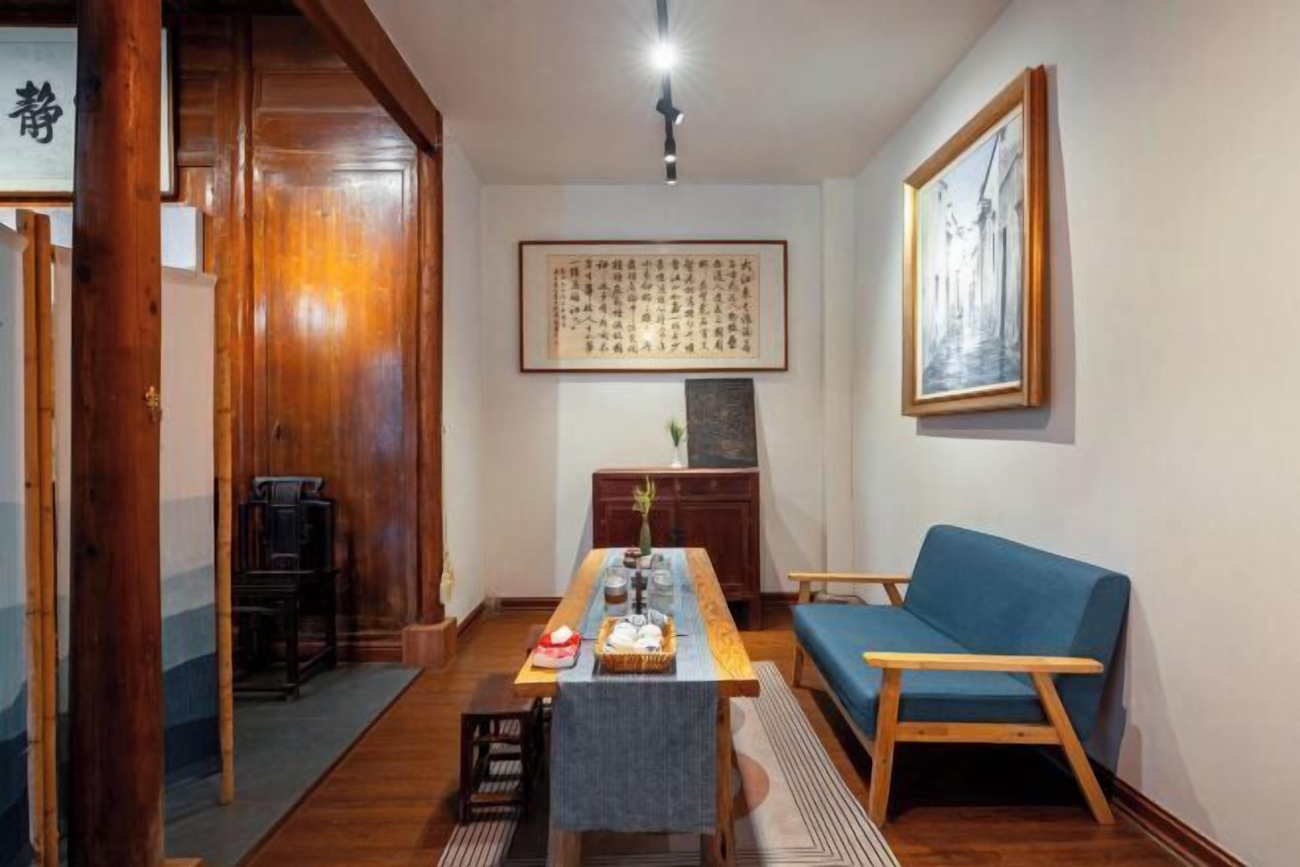 A traditional Japanese room with a tatami mat floor, a low wooden table with a tea set, a blue sofa, and a framed calligraphy piece on the wall.