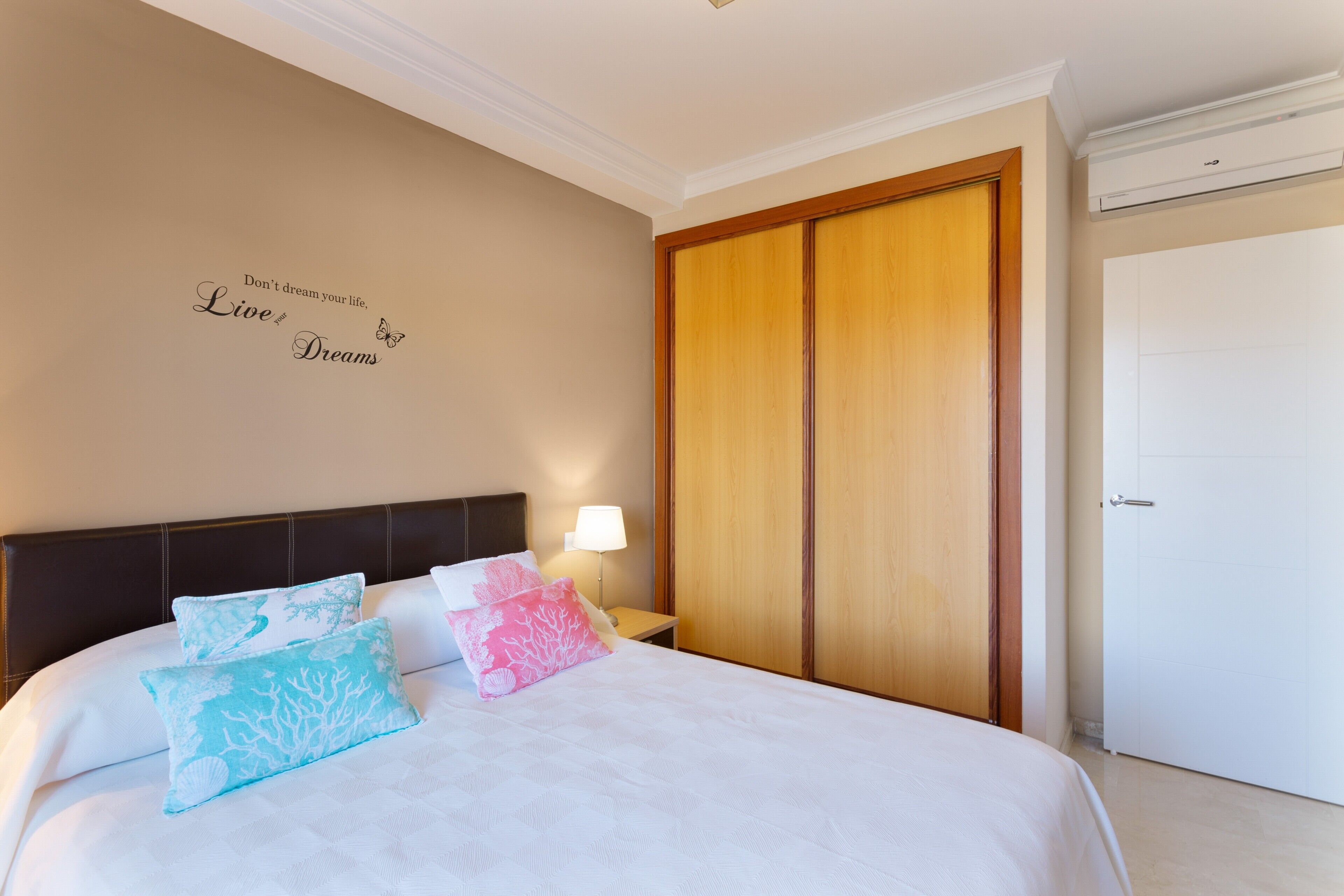 Een hotelkamer met een bed, een muur met motiverende tekst, een houten garderobe en een witte deur.