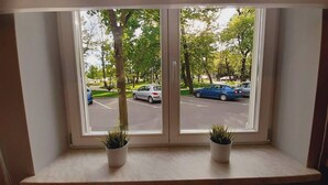 A window with two potted plants on a ledge, overlooking a parking lot with cars and trees.