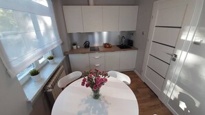 A modern kitchen with white cabinets, a round dining table with a vase of flowers, and a window providing natural light.