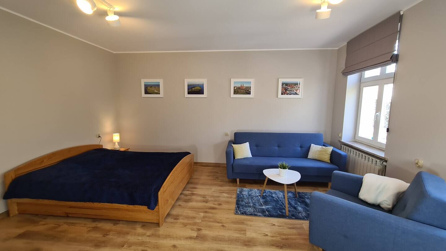 Een slaapkamer met een houten bed, een blauwe bank, een klein rond tafeltje en vier ingelijste foto’s aan de muur.