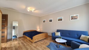 Un dormitorio moderno con una cama de madera, un sofá azul y una pequeña mesa blanca. Hay cuadros enmarcados en la pared y un espejo a la izquierda.