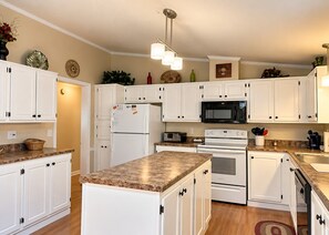 Una cocina con armarios blancos, un refrigerador, un microondas, un horno y una encimera de granito.