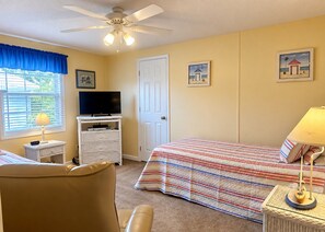 A hotel room with a bed, a television, a chair, a desk, and a ceiling fan.