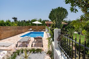 A pool area with lounge chairs, a white umbrella, and a cactus plant.