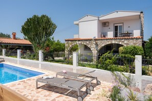 A modern villa with a swimming pool, sun loungers, and a stone archway.