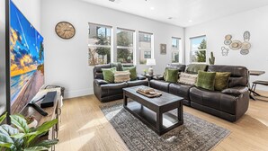 A modern living room with a large flat-screen TV, leather sofas, a coffee table, and a ceiling fan.