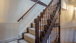 Een trap met houten spijlen en een leuning, betegelde treden en een witte radiator aan de muur.