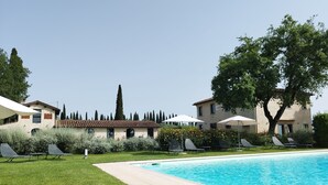 Una piscina con sillas de descanso y sombrillas, rodeada de césped y árboles bien cuidados.