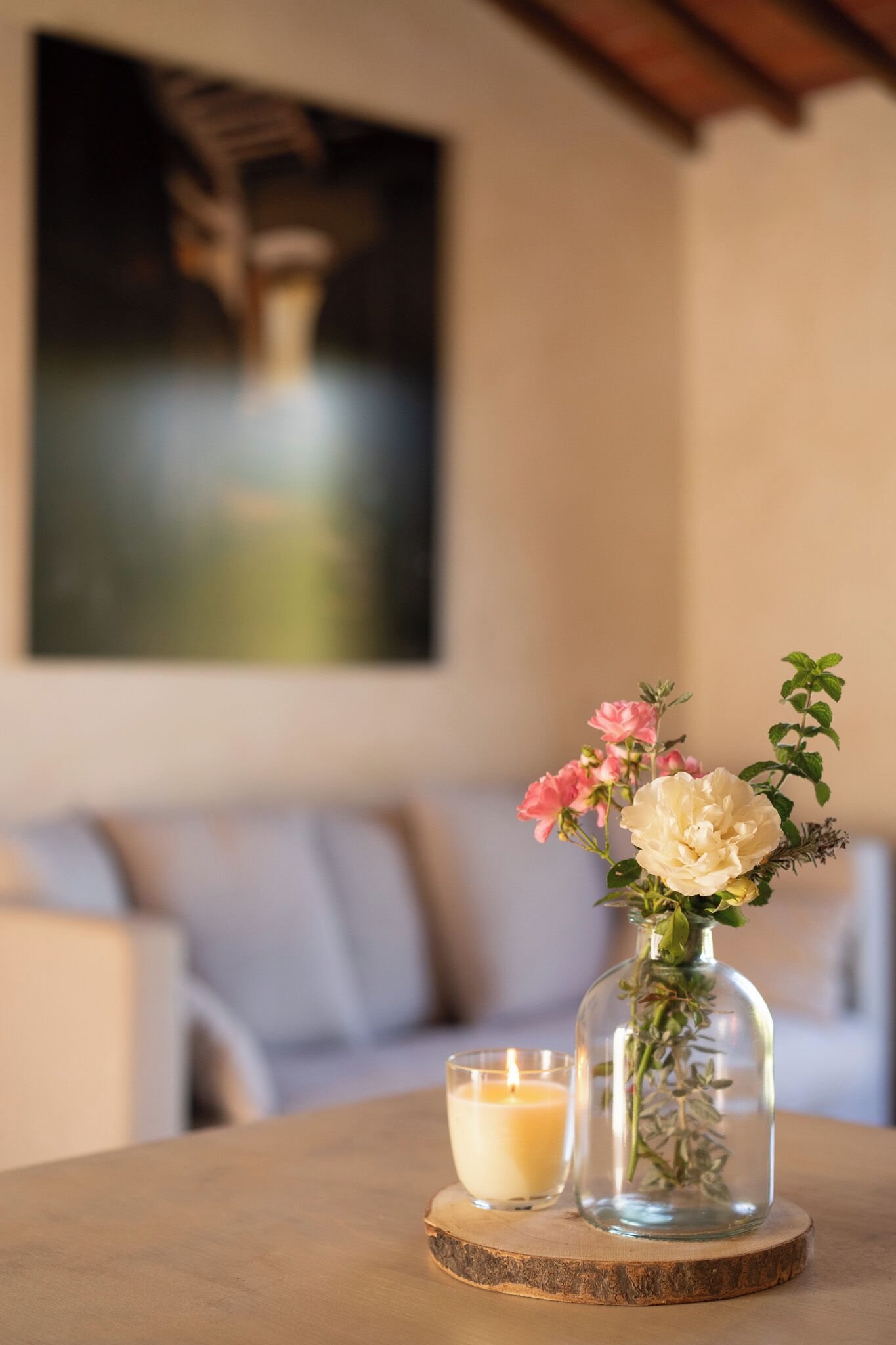 A table with a candle, a glass vase with flowers, and a wooden coaster.
