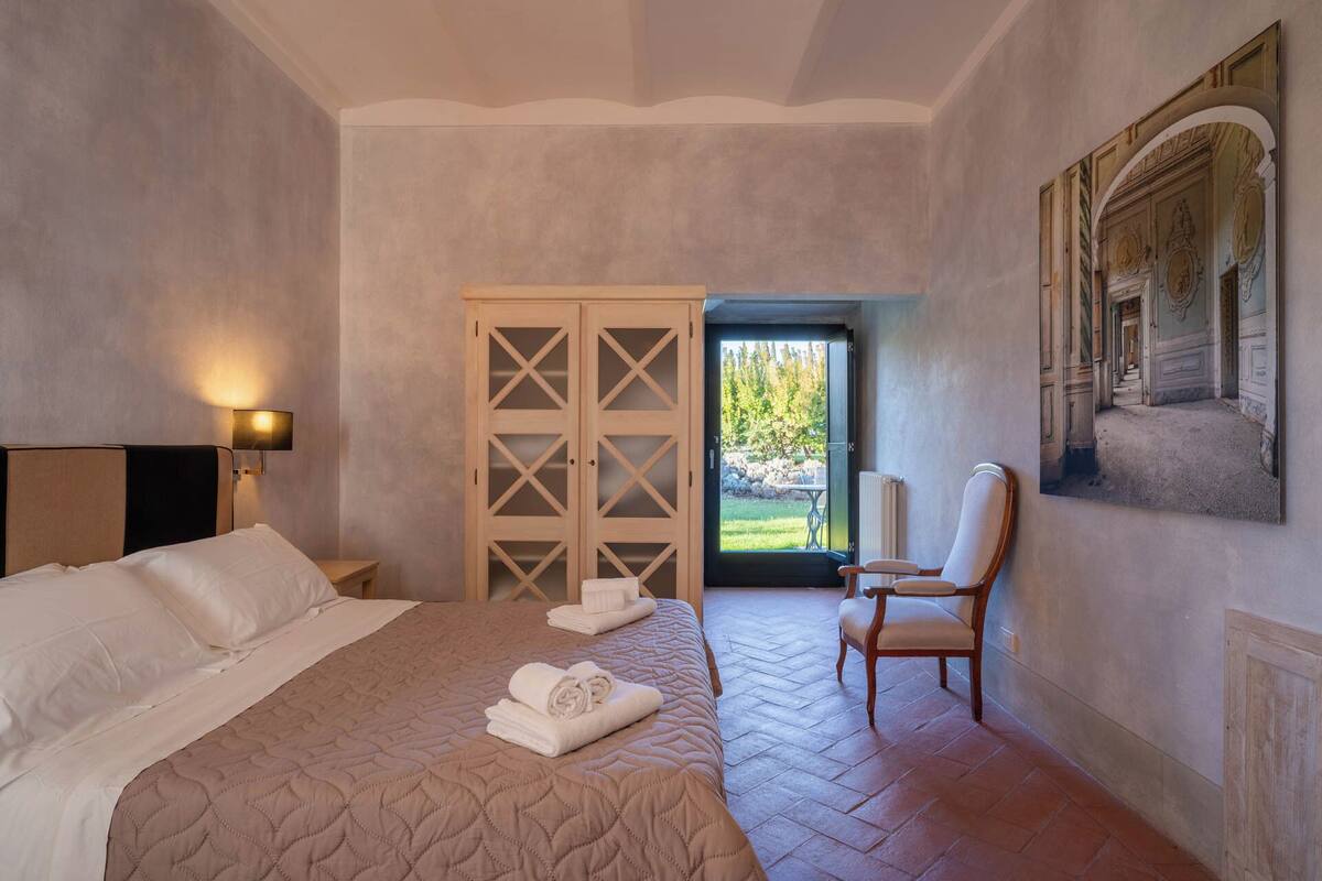 A hotel room with a bed, a chair, a wardrobe, and a view of the outdoors.