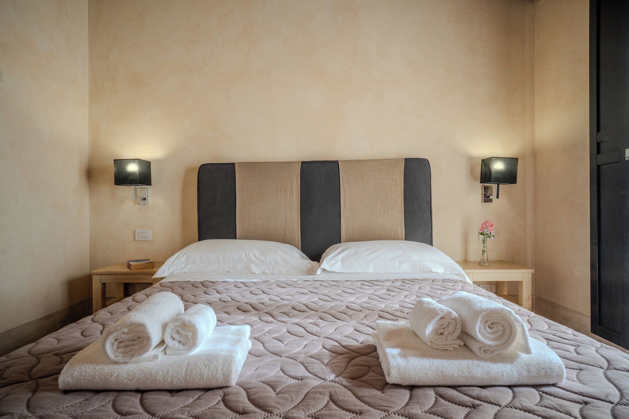 A hotel room with a large bed, two bedside tables, and two wall-mounted lamps.