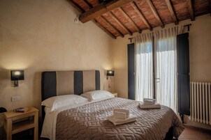 Un dormitorio con una cama grande, dos mesitas de noche, una lámpara de pared y una ventana con cortinas.