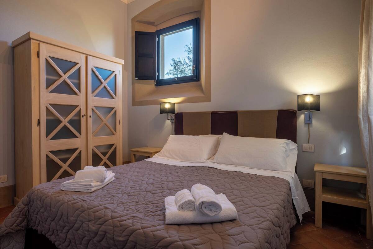 A bedroom with a bed, two nightstands, a wardrobe, and a window.
