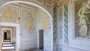 Un pasillo ornamentado con detalles arquitectónicos clásicos, incluyendo frescos y molduras decorativas.