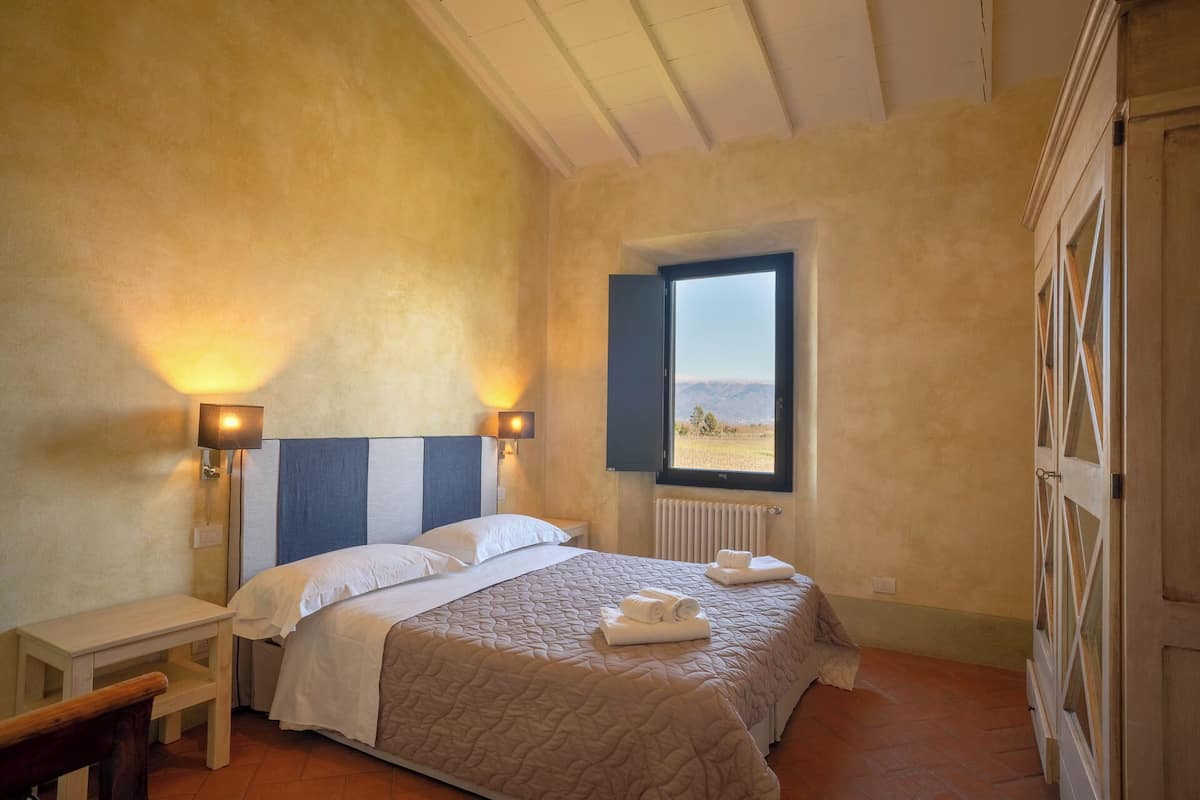 A bedroom with two beds, a window with a view, a bedside table, and a radiator.