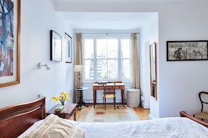 A bedroom with a bed, a desk, and a chair. There is a window with curtains, a radiator, and a lamp. - Elegant Flat - Notting Hill. Minutes from Hyde Park. (London)