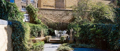 A courtyard with a brick wall, a small table with chairs, and dense foliage.