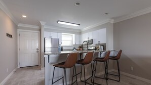 Uma cozinha moderna com armários brancos, uma geladeira de aço inoxidável e um espaço bar com banquetas.