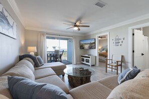 A living room with a glass coffee table, beige sofas, and a ceiling fan.