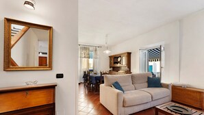 Een woonkamer met een bank, salontafel en een houten kast. Op de achtergrond is een eethoek met een tafel en stoelen.
