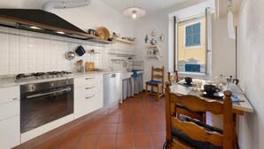 Een keuken met witte kastjes, een fornuis en een raam met blauwe luiken.