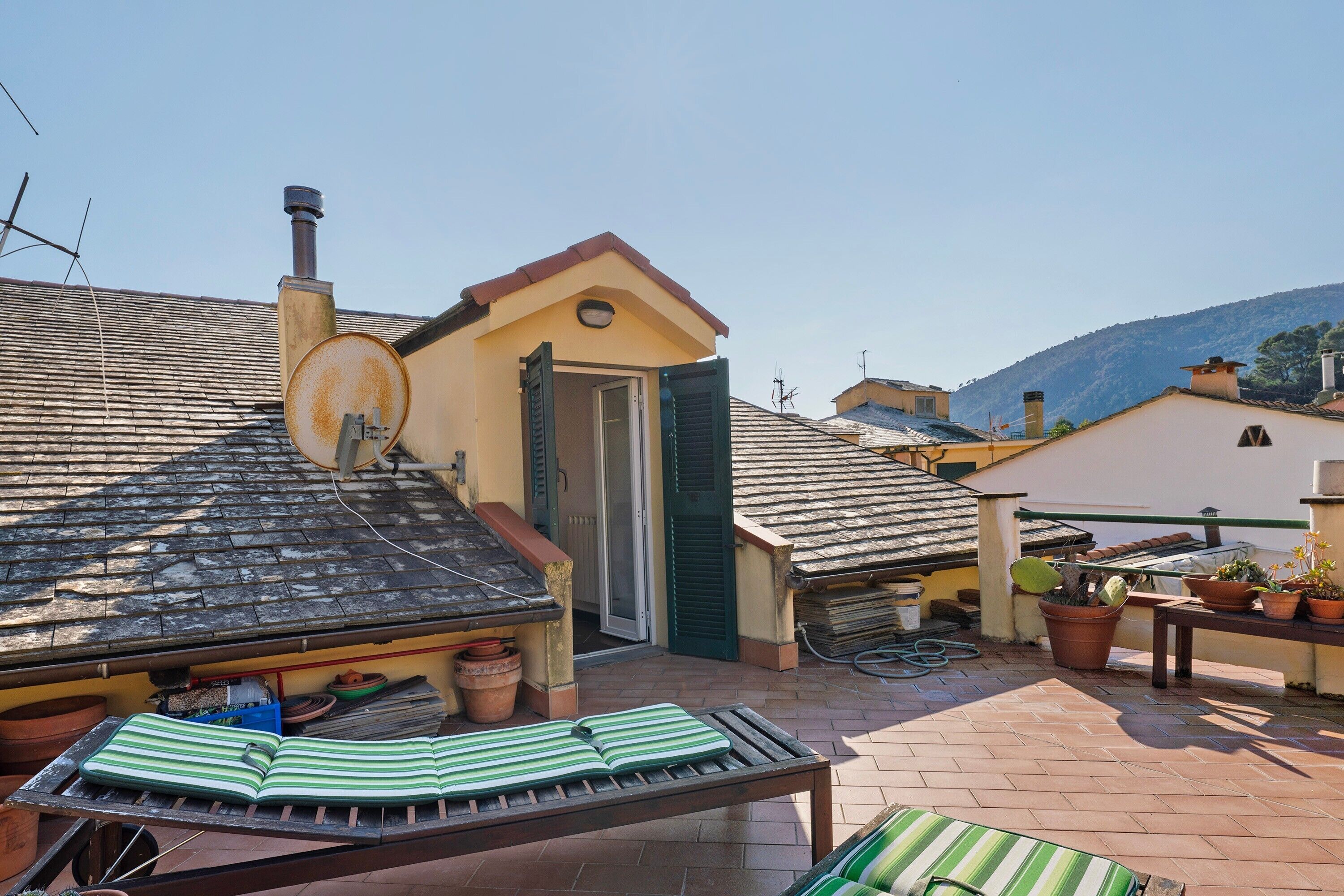 Eine Dachterrasse mit Liegestuhl, Topfpflanzen und einem Schornstein.