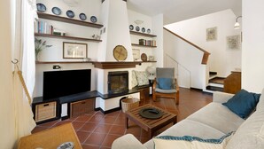 Een woonkamer met een open haard, televisie, bank en een boekenkast.