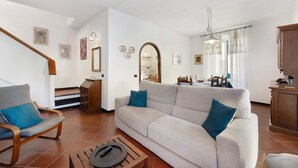 Een woonkamer met een bank, fauteuil, houten bijzettafeltje en een trap.
