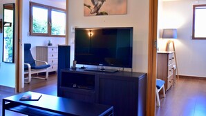 Una sala de estar con televisor de pantalla plana, una silla, una mesa, una lámpara y un cuadro de un pájaro.