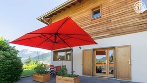 Una casa de madera con un paraguas rojo, macetas de madera y vistas a las montañas.