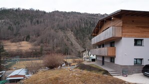 A modern building with a balcony, a parking area, and a mountainous backdrop. - Apartment 'Appartamento Rododendro' with Mountain View, Private Terrace and Wi-Fi (San Tomaso Agordino)