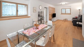 A modern living room with a dining area, wooden flooring, a flat-screen TV, and a grey sofa. - Apartment 'Appartamento Rododendro' with Mountain View, Private Terrace and Wi-Fi (San Tomaso Agordino)