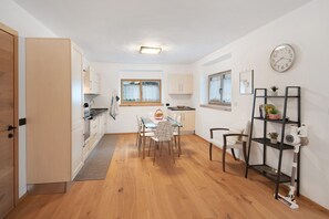 Une cuisine compacte avec des meubles en bois, une table à manger avec des chaises, une petite fenêtre et une horloge au mur.