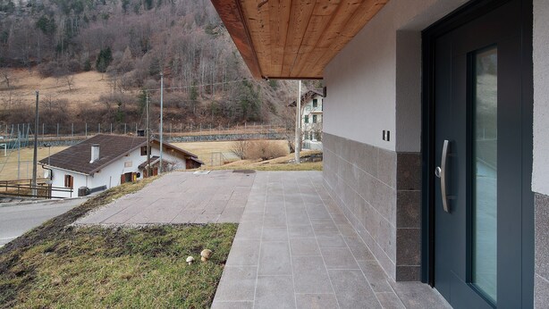 A building with a wooden overhang, a modern door, and a view of a hilly landscape. - Apartment 'Appartamento Rododendro' with Mountain View, Private Terrace and Wi-Fi (San Tomaso Agordino)