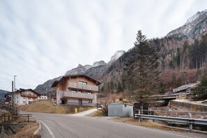 Un edificio de madera de varios pisos con balcones, una carretera en primer plano y montañas al fondo.